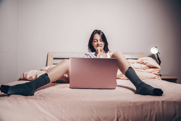 Молода дівчина азіатської веб-камери лежить перед ноутбуком з розстебнутими ногами. Захоплюється і показує свої чари. низька глибина фокусу, вибірковий фокус.. - Фото, зображення
