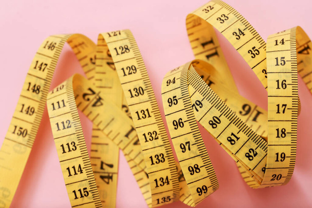 tape maatregel voor zwaarlijvige mensen op een roze achtergrond zachte focus - Foto, afbeelding