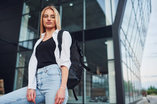 Beautiful blonde in casual clothes is outdoors at sunny daytime against business building. - Zdjęcie, obraz