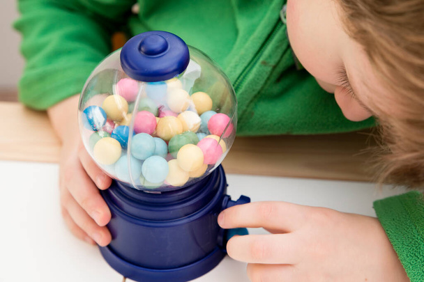 Beautiful boy plays with candy machine. Gumball Machine toy with colorful balls. Sweet childhood dream. Reward for good job done. - Photo, Image