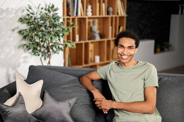 Ethnic man sitting on the sofa and smiling, in a normal t shirt, feeling comfort and relaxation, at an interview - 写真・画像