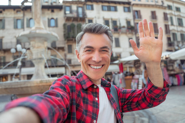 Man smiling at camera raising hand in greeting - Фото, изображение