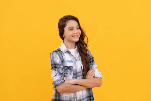 cheerful teen girl in checkered shirt and with long curly hair on yellow background - Fotó, kép