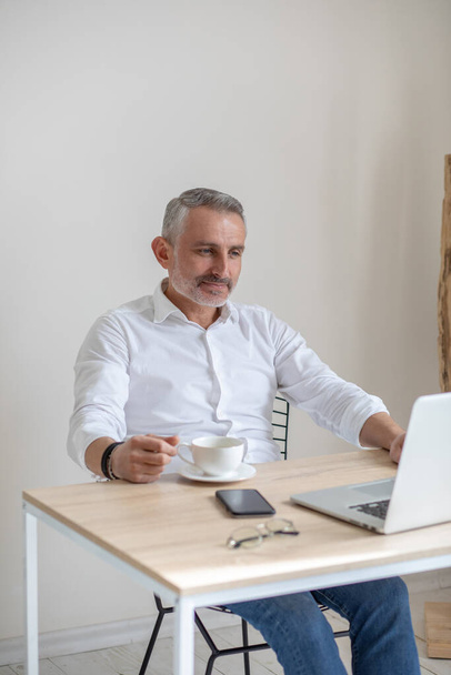 Smiling man with coffee working on laptop - Zdjęcie, obraz