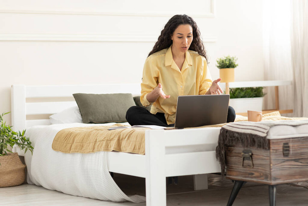 Dizüstü bilgisayar kullanan bir kadın yatakta oturmuş video görüşmesi yapıyor. - Fotoğraf, Görsel