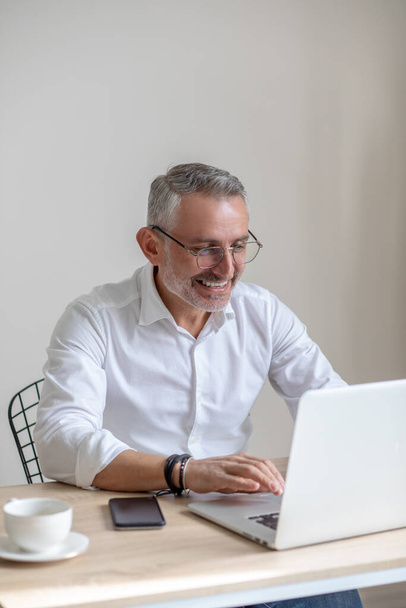 Smiling man in glasses typing on laptop - Фото, изображение