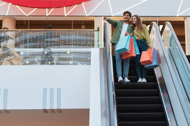 Χαρούμενο ζευγάρι στέκεται στις κινούμενες σκάλες στο σύγχρονο εμπορικό κέντρο - Φωτογραφία, εικόνα