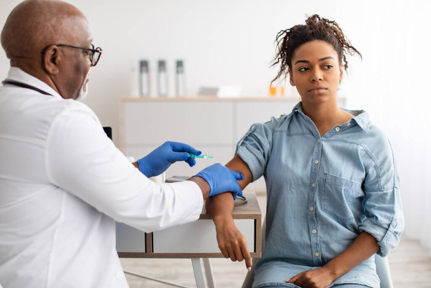 Black Woman Receiving Vaccine Injection Sitting With Doctor Indoor - Foto, imagen