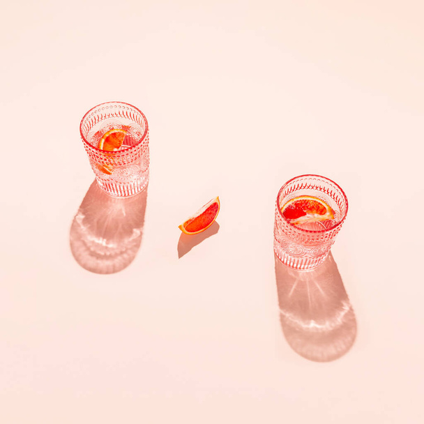 Composição criativa feita de dois glasse com coquetel ou limonada em fundo pastel bege com lóbulo de laranja sangrenta. Conceito de refresco de verão. Deitado ao sol. Estilo mínimo. Vista superior - Foto, Imagem