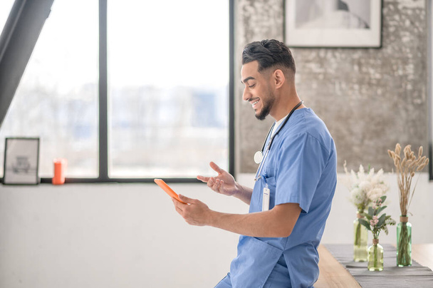 Pleased healthcare worker using his gadget indoors - Photo, Image