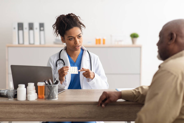 Kobieta czarny lekarz pokazuje pigułki dla pacjenta płci męskiej - Zdjęcie, obraz