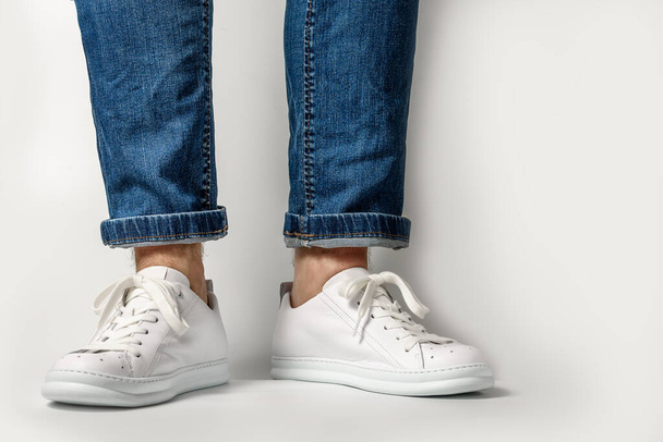 Man in Stylis Nieuwe Witte Sneakers en jeans Over Witte Achtergrond. Horizontaal beeld - Foto, afbeelding