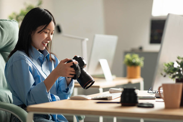 Портрет азіатської жінки тримає фотоапарат дивлячись на екран
 - Фото, зображення