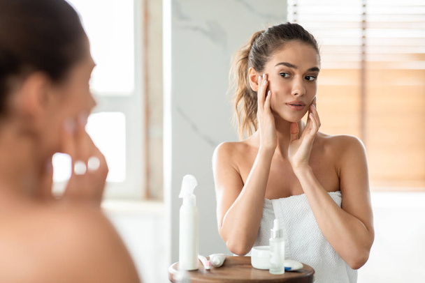 Femme touchant visage soignant pour la peau lisse parfaite dans la salle de bain - Photo, image