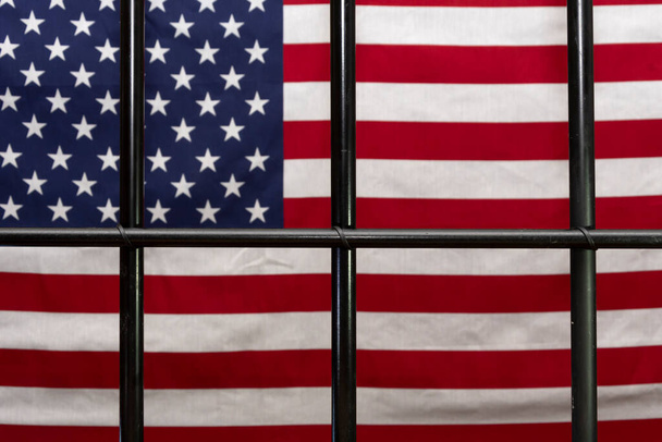 La griglia della cella di detenzione sullo sfondo della bandiera americana. Concetto: sessione del tribunale, processo della giuria, condanna. - Foto, immagini