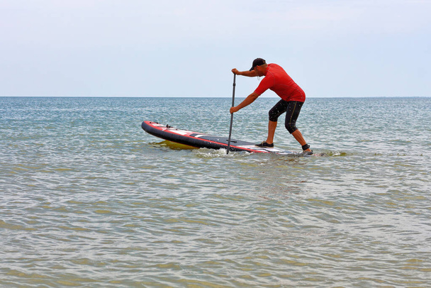 Радостный человек тренируется на доске для внедорожников на море. Встать на весло посадки - Фото, изображение