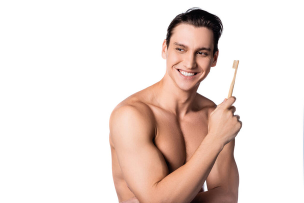 uomo muscoloso senza maglietta con spazzolino da denti sorridente e distogliendo lo sguardo isolato sul bianco - Foto, immagini