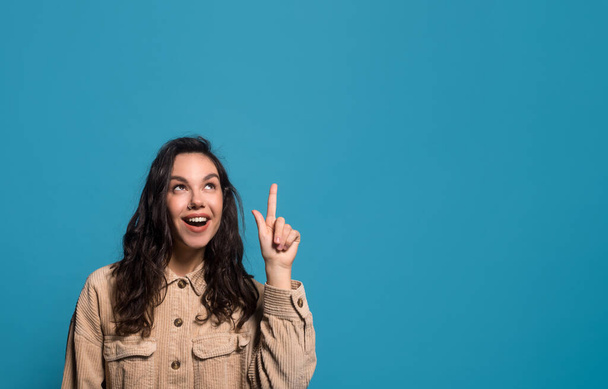 Glad surprised millennial european brunette female in casual got idea, showing finger up on blank space - Фото, изображение