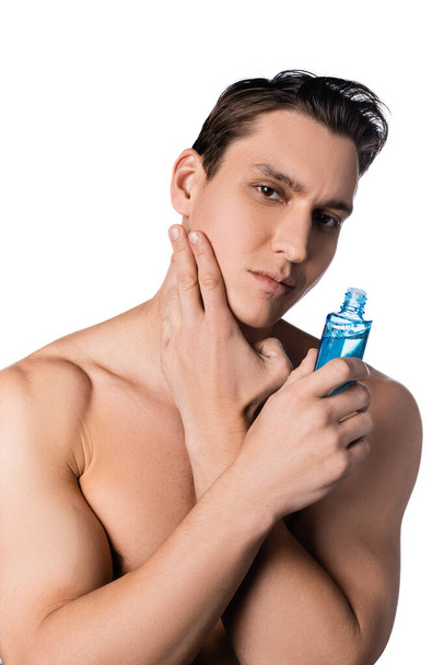 brunette man with naked shoulders applying after shave lotion isolated on white - Foto, Imagem