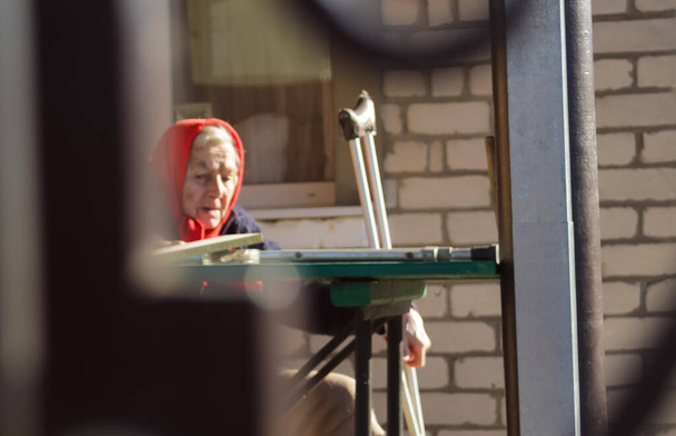 Defocus ukrainian elderly woman in red shawl with crutches sitting outside. Woman 85 years old. Alone person. Blurred. Sad people. Dementia, memory. Copy space. Frame. Out of focus. - Foto, Imagen