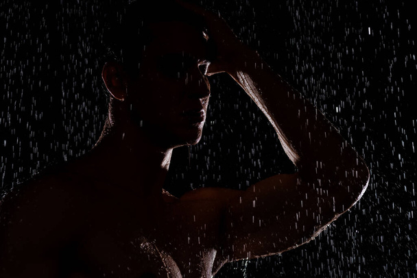 silueta del hombre bajo gotas de agua cayendo sobre fondo negro - Foto, imagen