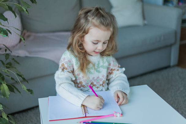 Little curly-haired cute blue-eyed girl 4 years old in a cozy house. Portrait of a happy child. Home school. - Foto, Imagen