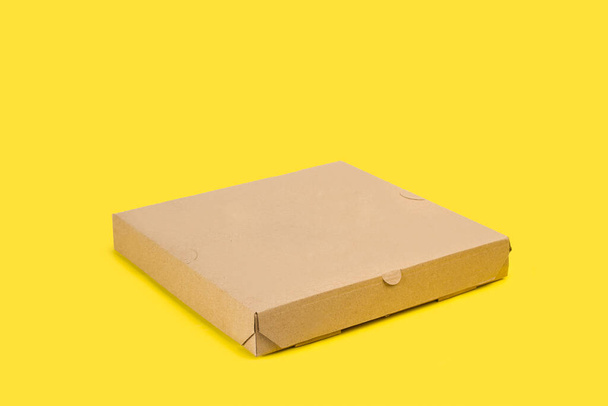 Una scatola di pizza di cartone marrone su uno sfondo giallo con spazio di copia - Foto, immagini