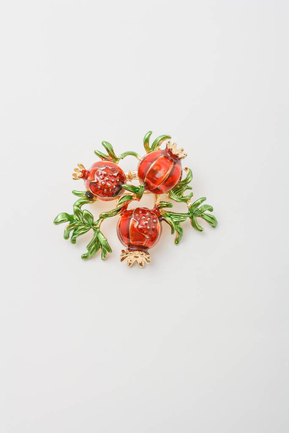 Metallic brooch in shape of three pomegranate fruits with green leaves, pin on white background, bijouterie, jewelry close up - Φωτογραφία, εικόνα