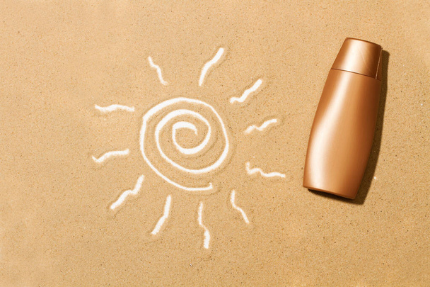 A sun tan lotion bottle and a drawing of the sun on the sand - Фото, изображение
