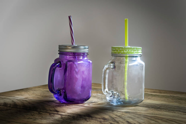 Tasses à boire en verre avec couvercles et pailles assises sur une table en bois avec fond blanc. - Photo, image