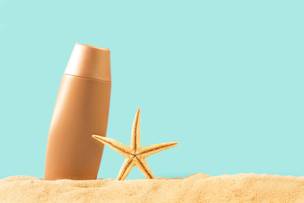 Une bouteille de crème solaire orange et une étoile de mer sur le sable et sur un fond bleu - Photo, image