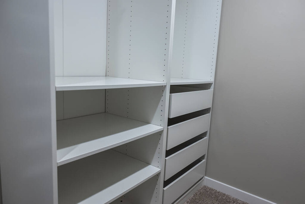 Blick auf hohe, weiße Schränke und Schubladen in einem schmalen begehbaren Kleiderschrank in einem Schlafzimmer - Foto, Bild