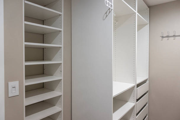 View of tall, white cabinets and drawers inside a narrow walk in closet inside a master bedroom - Zdjęcie, obraz