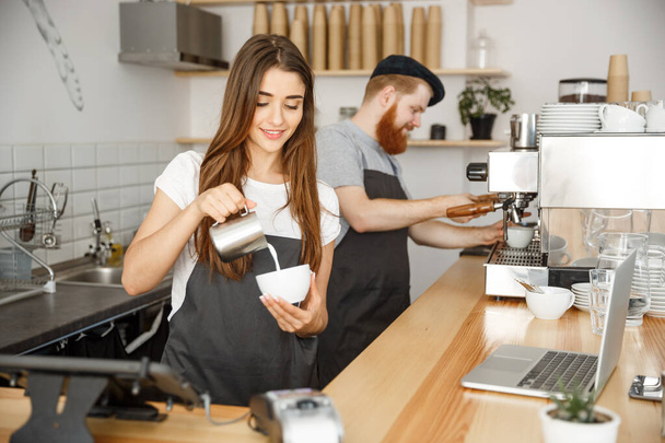 Coffee Business Concept - крупним планом леді-бариста в фартусі, що готує і заливає молоко в гарячу чашку, стоячи в кафе
. - Фото, зображення