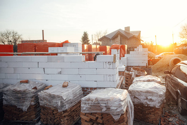 Autoclaved aerated blocks on concrete foundation and bricks in evening light, process of house building. Stacks of white aerated blocks for laying. Building materials at construction site - Foto, Imagen