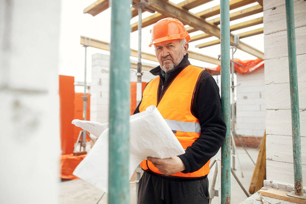 Vezető férfi művezető keménykalapban ellenőrzi az új modern ház terveit. Építőmérnök vagy építőmunkás, aki az építkezésen terveket nézegeti. Fénymásolási hely - Fotó, kép