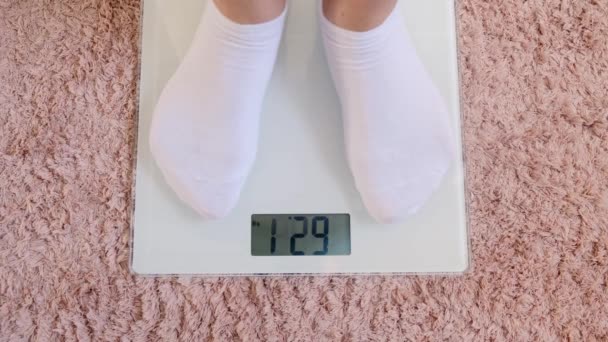 piernas de mujer en calcetines blancos de pie en balanzas digitales para comprobar el peso en el suelo en la habitación. - Metraje, vídeo