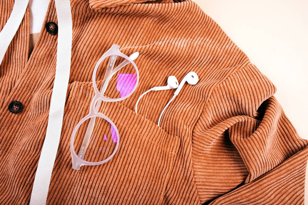 Trendy fall fashion flatlay with hoodie, brown corduroy shirt, earphones and glasses isolated on beige background. - Φωτογραφία, εικόνα
