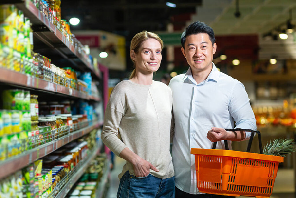 Happy married couple Asian man and woman looking at camera and smiling in grocery supermarket, choosing goods - Фото, зображення