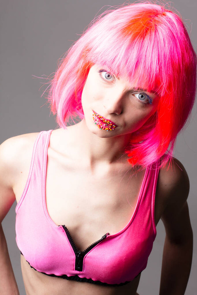 Imagem de mulher bonita animado na peruca rindo enquanto posando com doces isolados sobre fundo rosa
 - Foto, Imagem