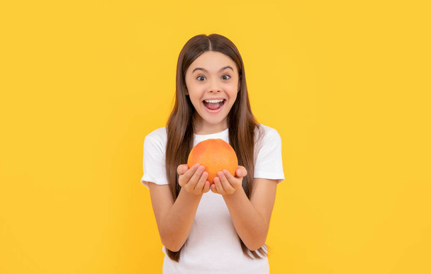 užaslé dítě držet grapefruit na žlutém pozadí, zdraví - Fotografie, Obrázek
