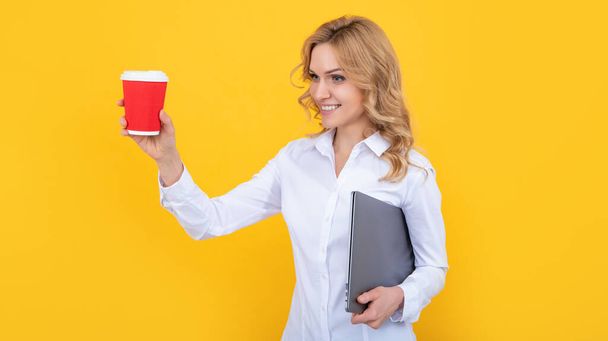 fröhliche blonde Frau mit Kaffeetasse und Computer auf gelbem Hintergrund - Foto, Bild