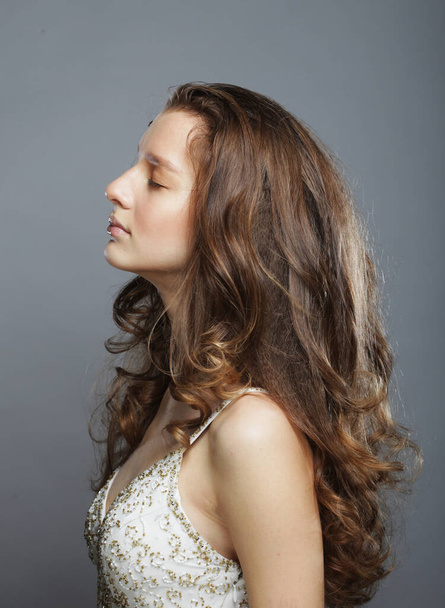 Adorable young female model with long curly hair in white dress posing in profile, purity and innocence - Foto, imagen