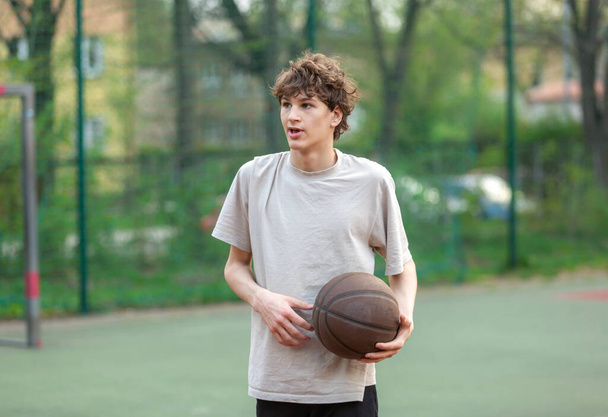 Mignon jeune adolescent en t-shirt blanc avec une balle joue au basket-ball. Sport, passe-temps, mode de vie actif pour les garçons - Photo, image