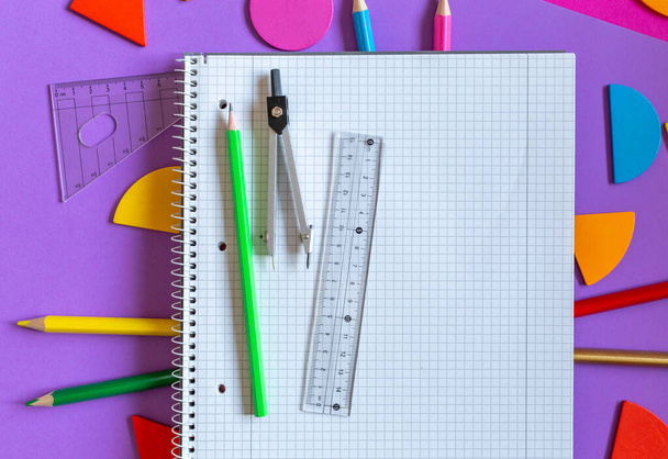 紫色の背景に学校の文房具。カラフルな数学の分数、支配者、紫色の背景に開いたノートパッド。子供のための面白い、楽しい数学。教育、学校の概念に戻る - 写真・画像