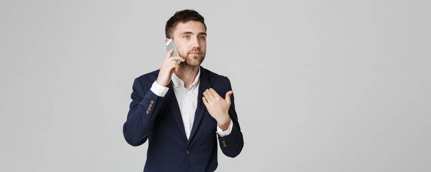 Business Concept - Portrait young handsome angry business man in suit talking on phone looking at camera. White background. - Foto, Bild