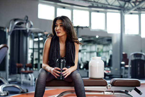 Młoda aktywna kobieta robi sobie przerwę w siłowni i pije shake 'a proteinowego. - Zdjęcie, obraz
