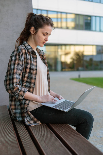 Front view. A girl in a shirt with a laptop on the street working. Remote work. conducting online video calls. Freelance girl. - Foto, Imagen