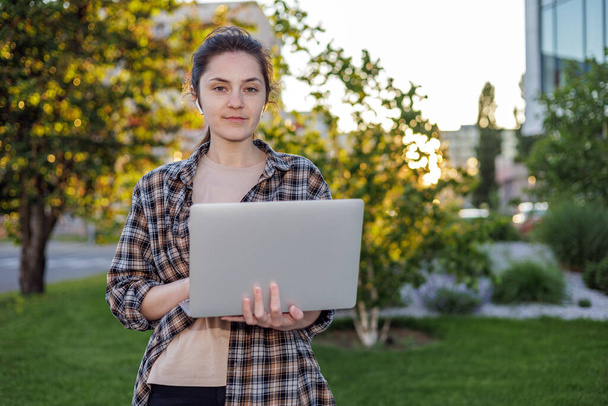 Előre nézz. Egy lány egy pólóban egy laptoppal az utcán dolgozik. Távoli munka. online videohívások lebonyolítása. Szabadúszó lány. - Fotó, kép