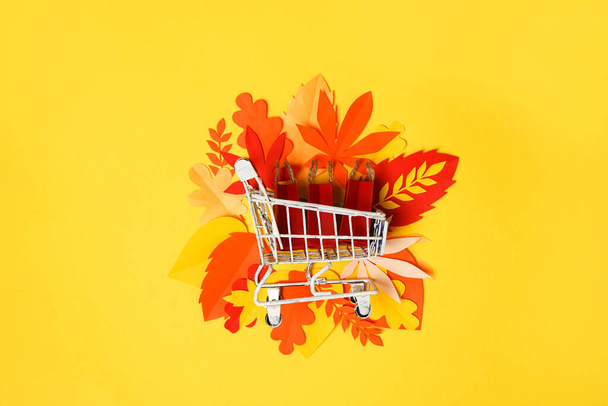 autumn shopping grocery cart with paper falling leaves on yellow background. Concept Autumn sale - Photo, Image